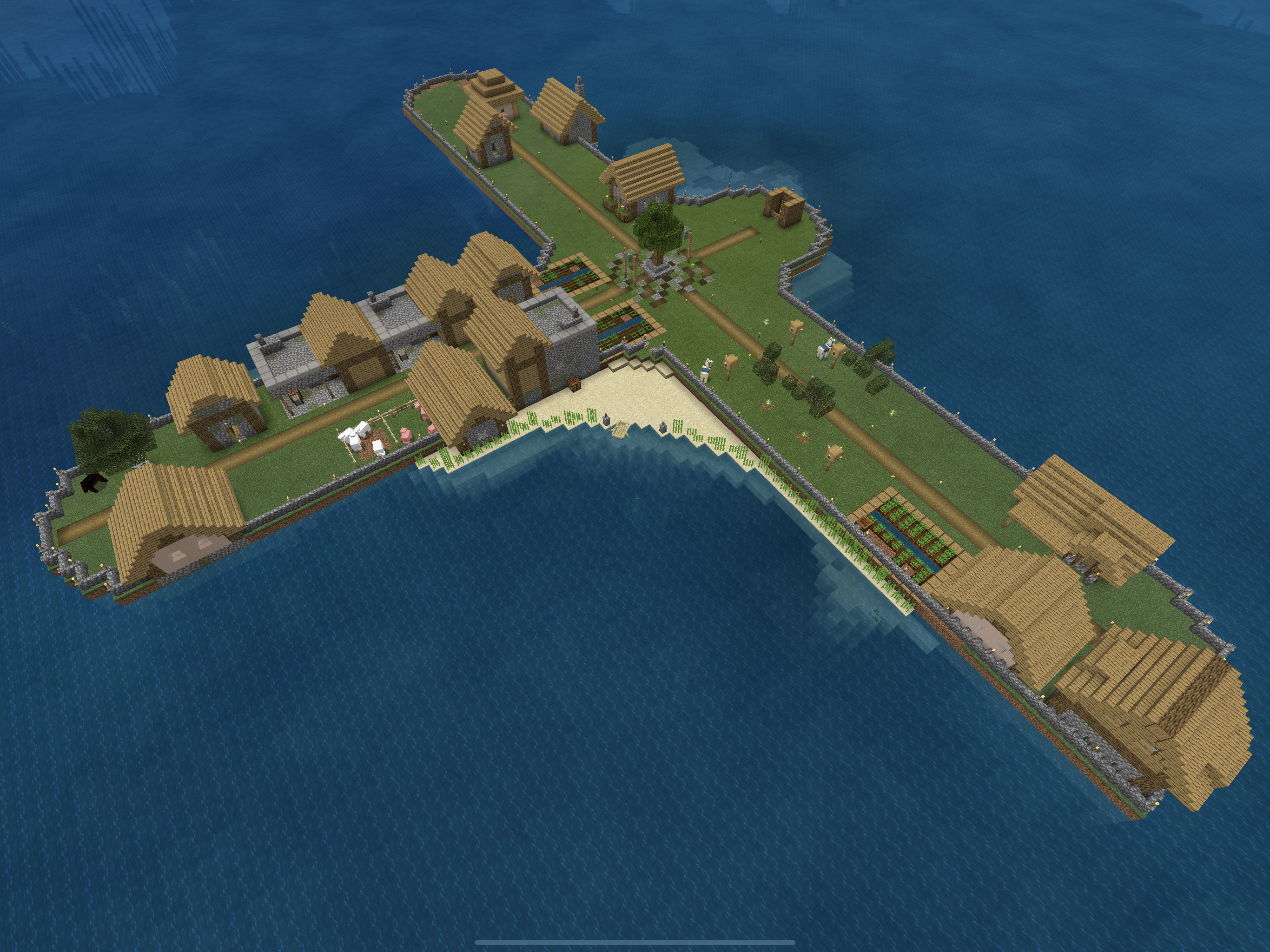 Minecraft screenshot featuring an aerial shot of a T-shaped island with a village on it and walls around the perimeter.