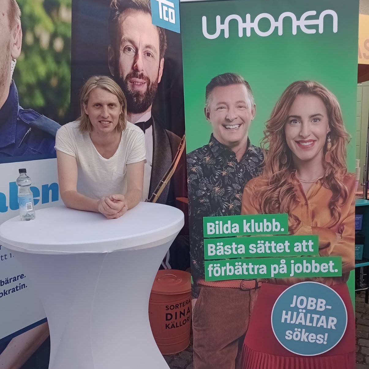 
    Person stood smiling at a booth at a conference. Next to them is a banner
    for the Swedish trade union “Unionen” with a slogan encouraging people to
    organise unions at their own workplaces.
  