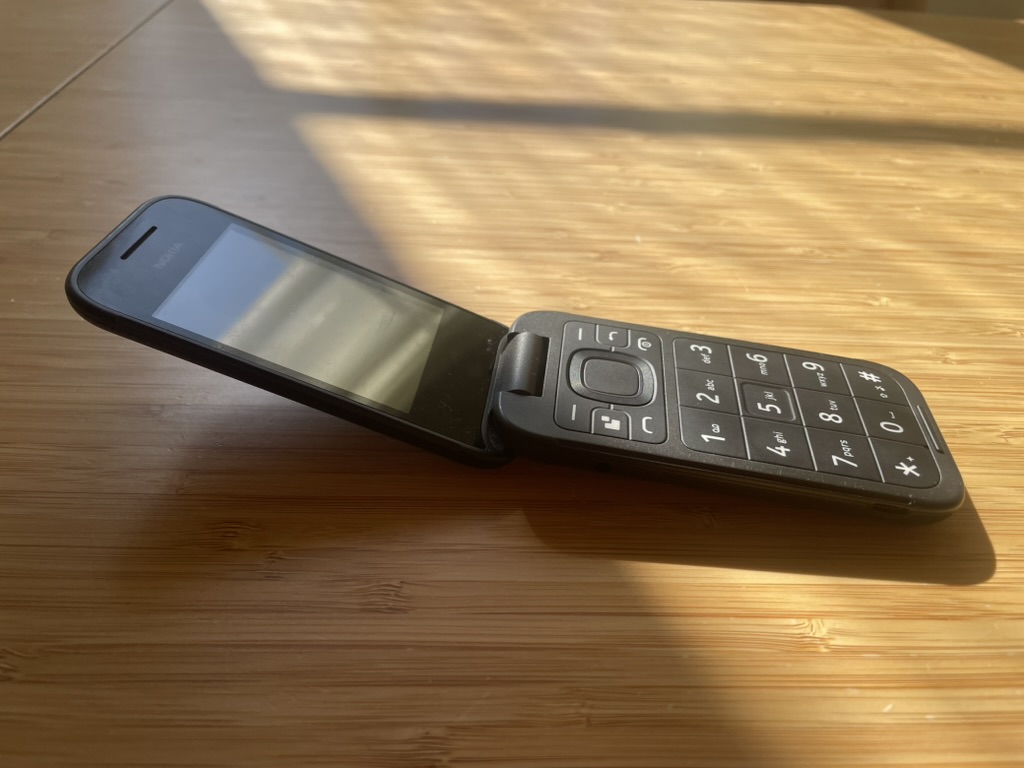 Black flip phone on a sunlit wooden table