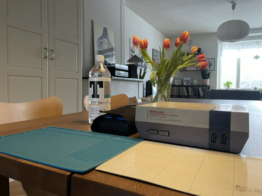 NES on a wooden table next to a repair kit, bottle of isopropyl alcohol, and some electronics mats
