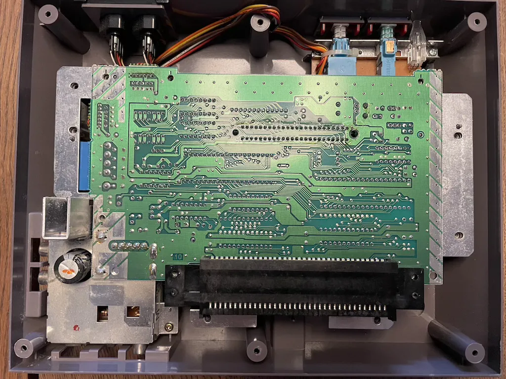 Top-down view of a NES with the cover removed. A large green circuit board with some wires and other components around it.