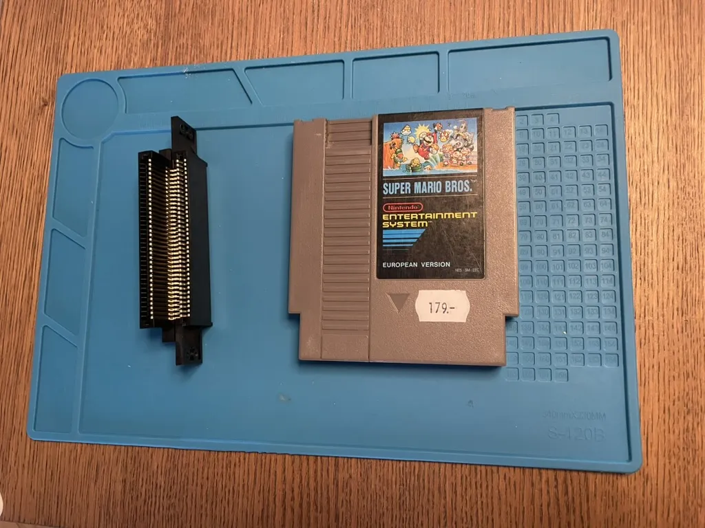A 72 pin connector from a NES and a Super Mario Bros cartridge together on a blue electronics work mat