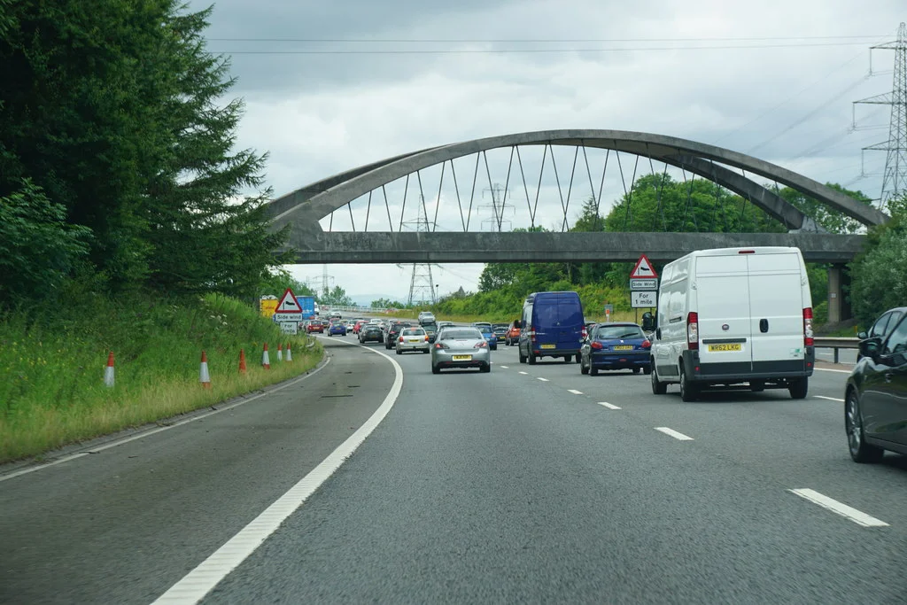 Motorway scene with a bridge in the middle distance. Traffic is heavy.