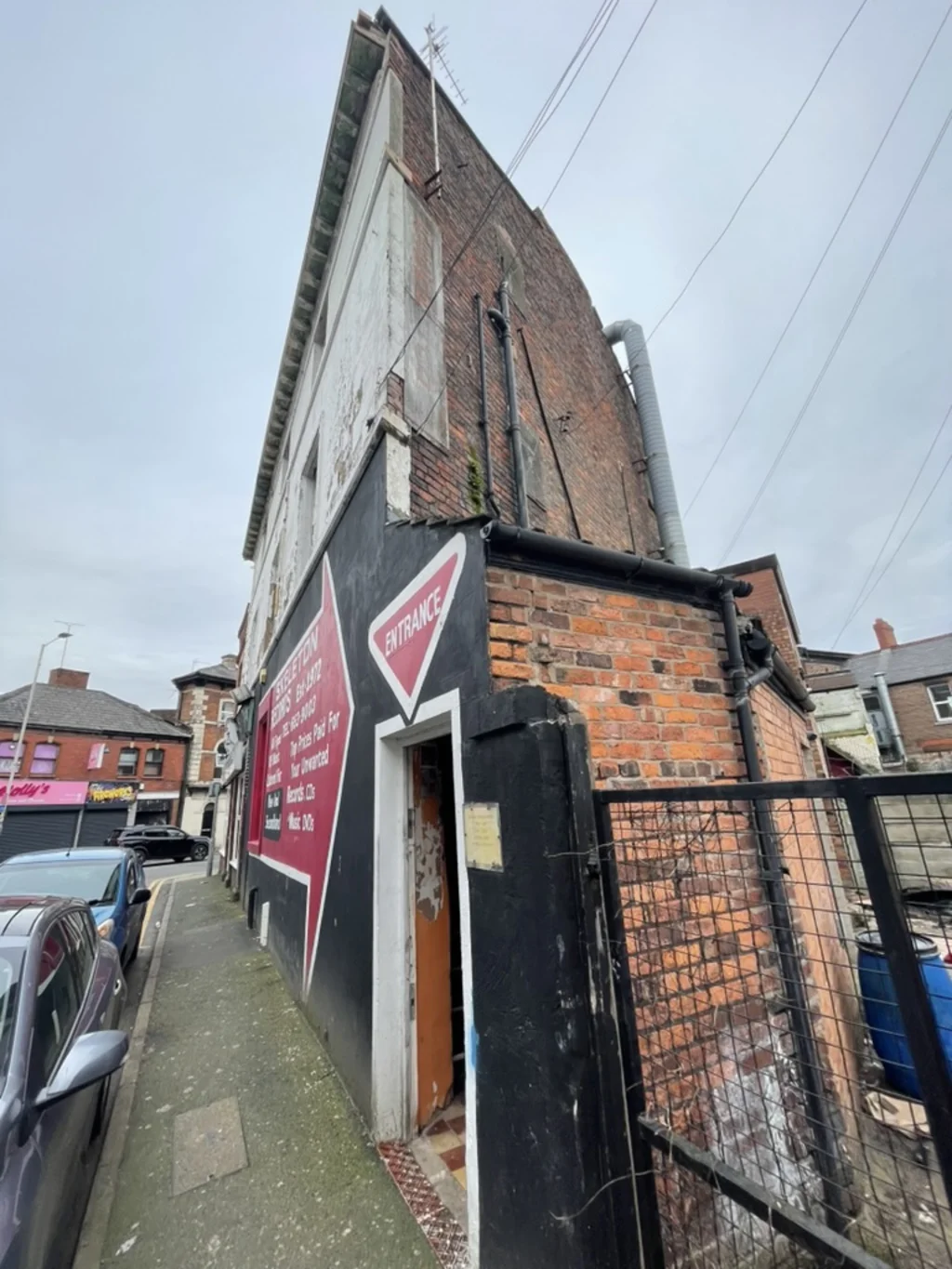 Red brick building with shop signage on the front and a red entrance sign pointing down at the door.