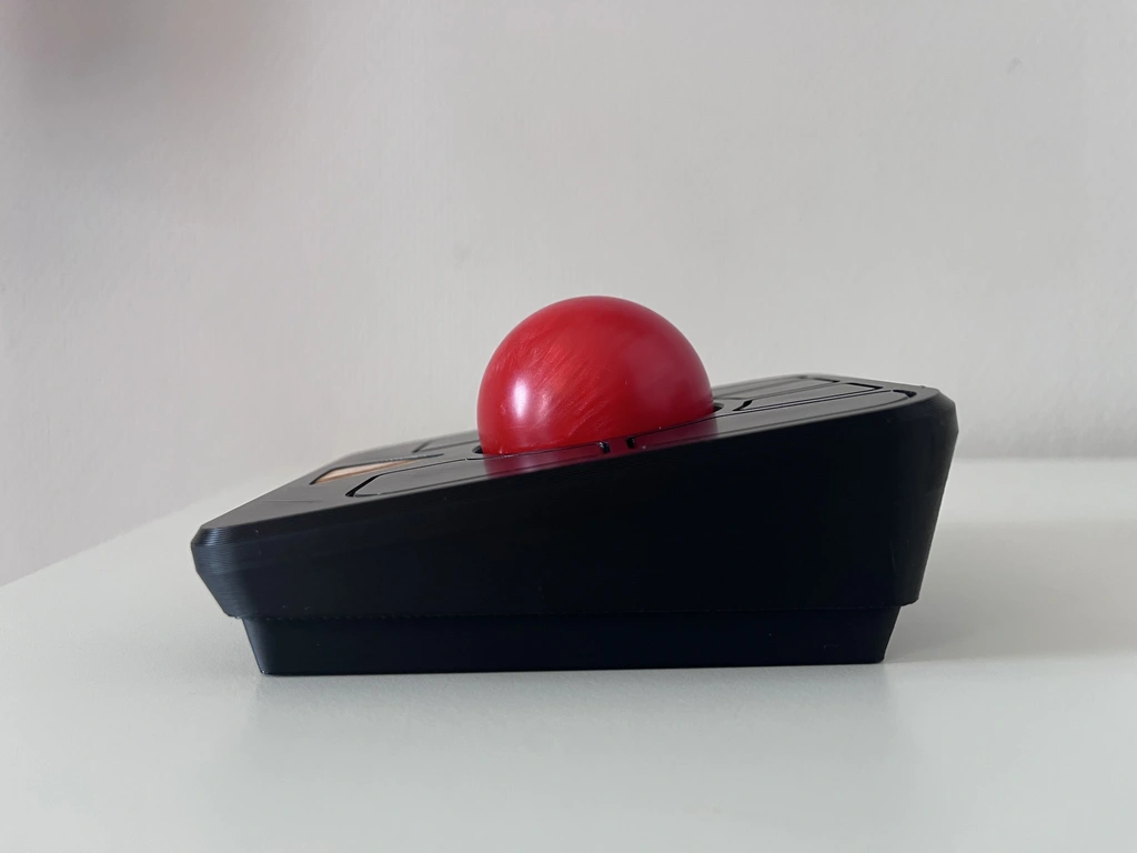 A side view of a trackball mouse with a black case and a red ball.