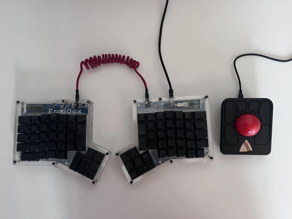 A black trackball mouse next to an 'Ergodox'-branded split keyboard.